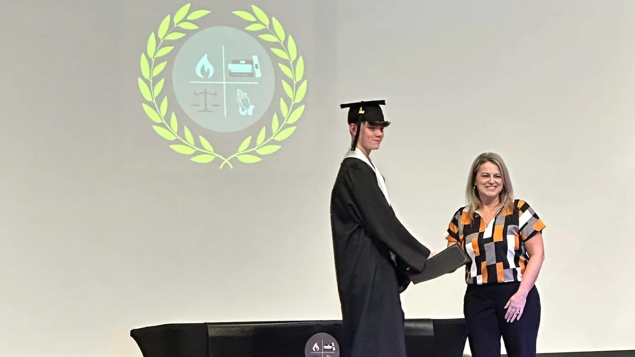 An HPCA graduate receiving a diploma from a teacher on the graduation stage