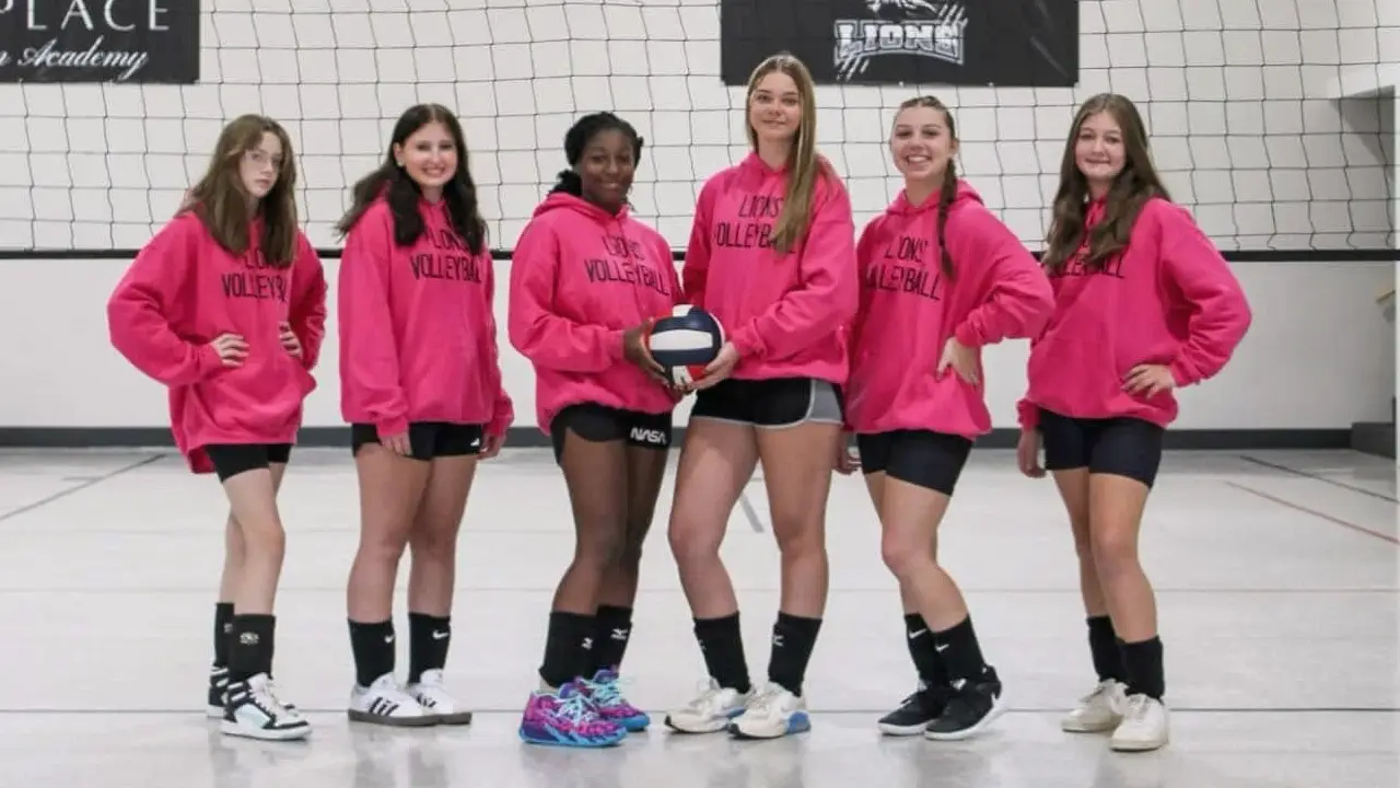 The HPCA Lions volleyball team in pink team hoodies on the school court